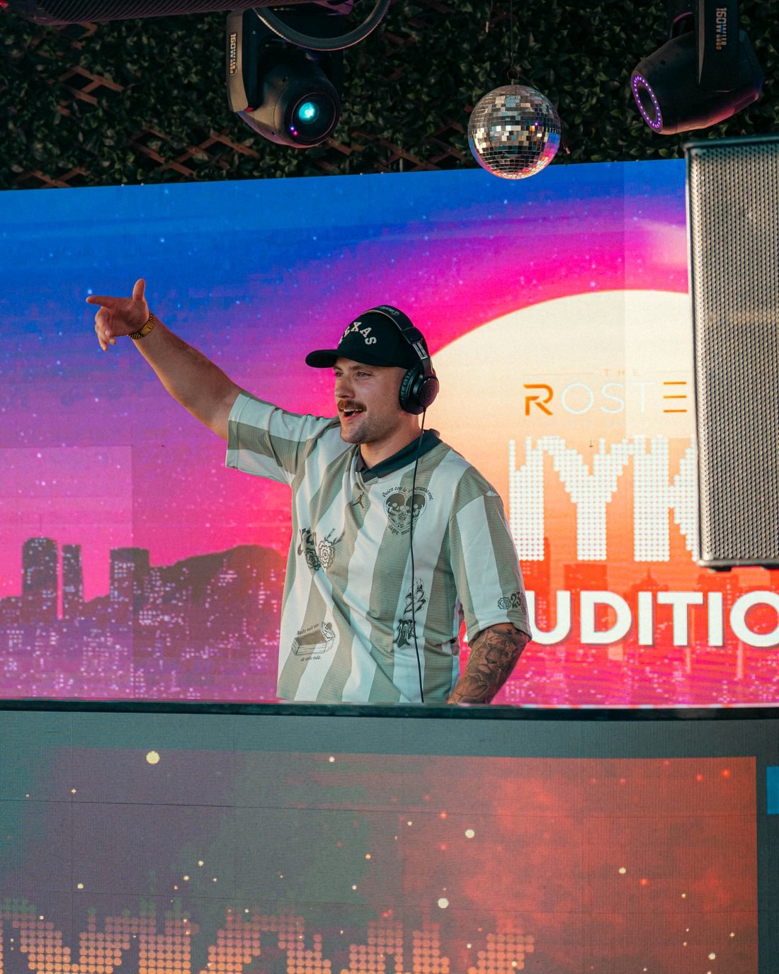 B.Y. behind the decks at the IYKYK live DJ auditions, pointing at the crowd.
